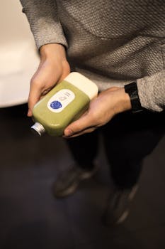 Hands holding a bottled green juice indoors in New York City, emphasizing health and wellness.