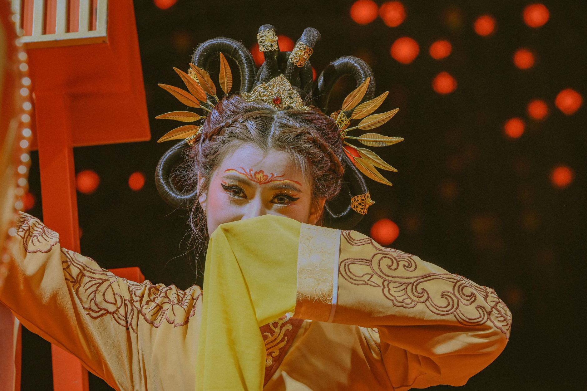 A Chinese performer in traditional dress with intricate hairpiece and face paint on stage.