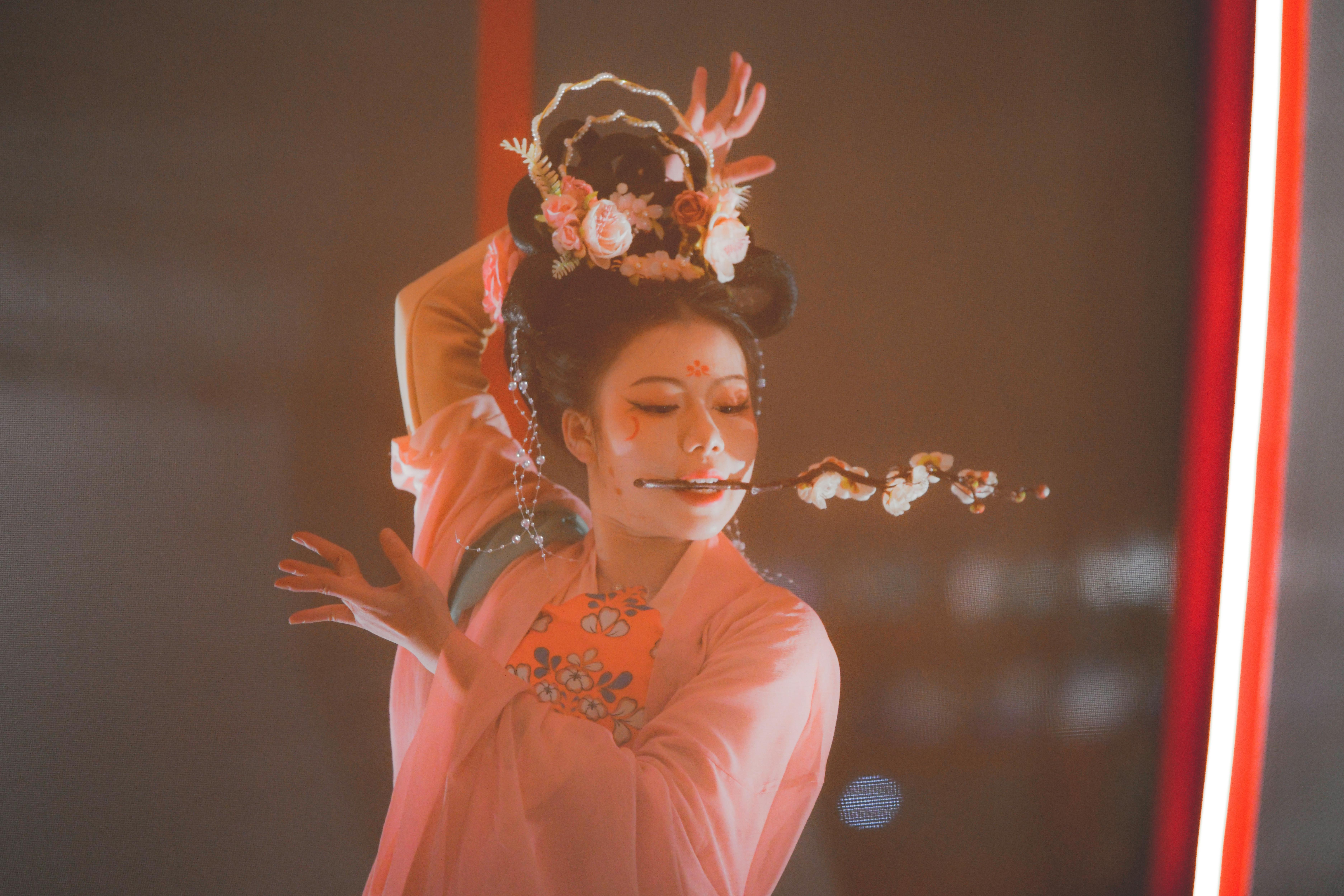 Free A woman in pink traditional clothing performing a graceful dance with flowers in her hair. Stock Photo