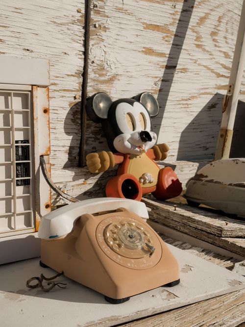 Free An old rotary dial telephone with a vintage toy on a weathered wooden surface in sunlight. Stock Photo