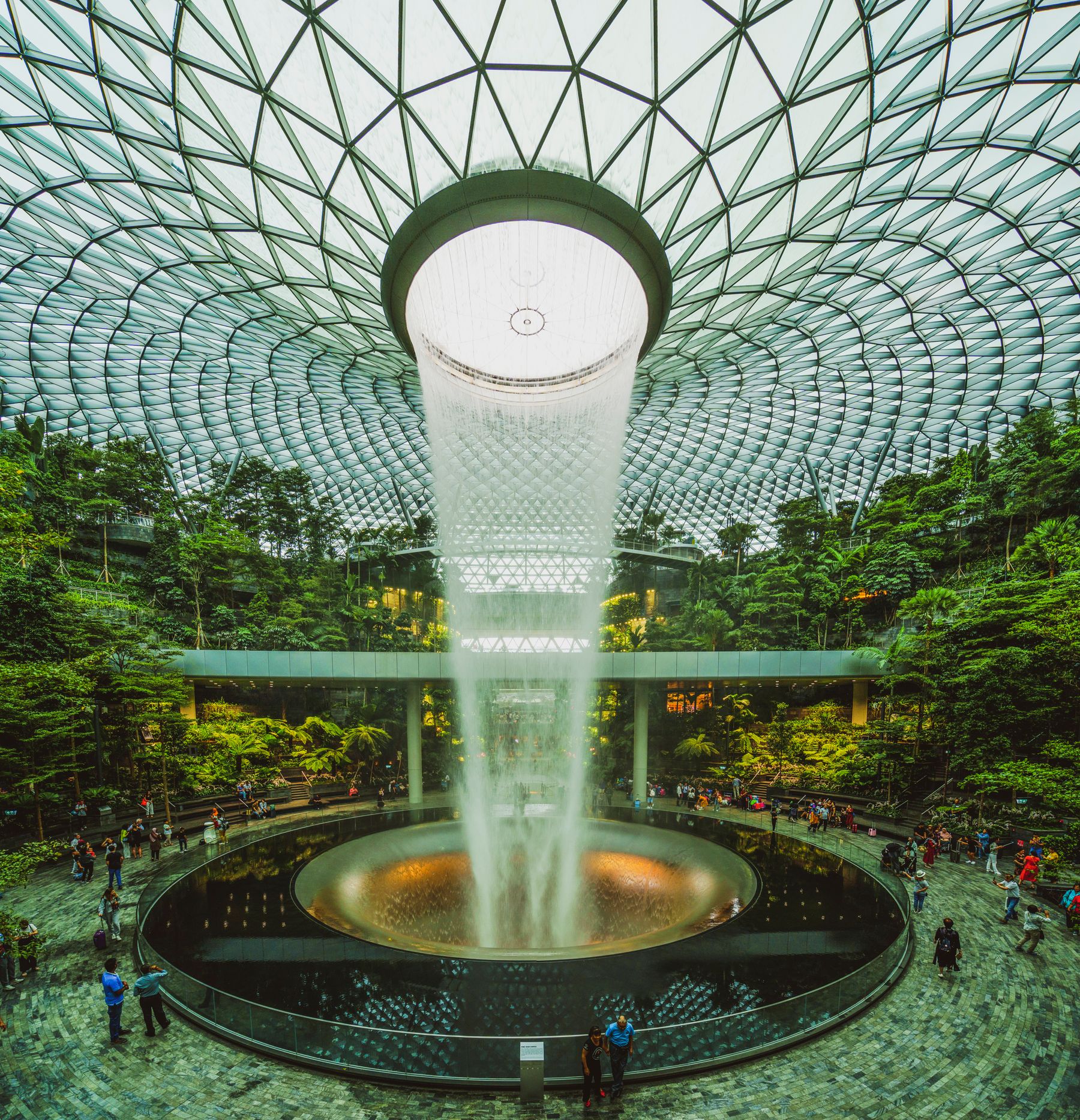 Travelers and luggage beneath Jewel Changi Airport's Rain Vortex