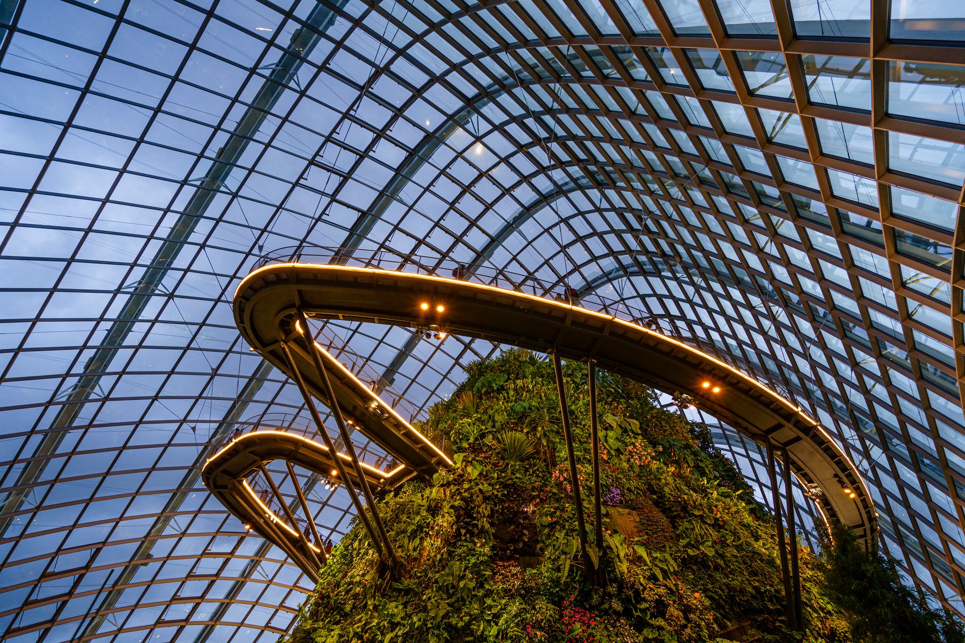 Interior view of a futuristic botanical garden with lush plants and a glass roof.