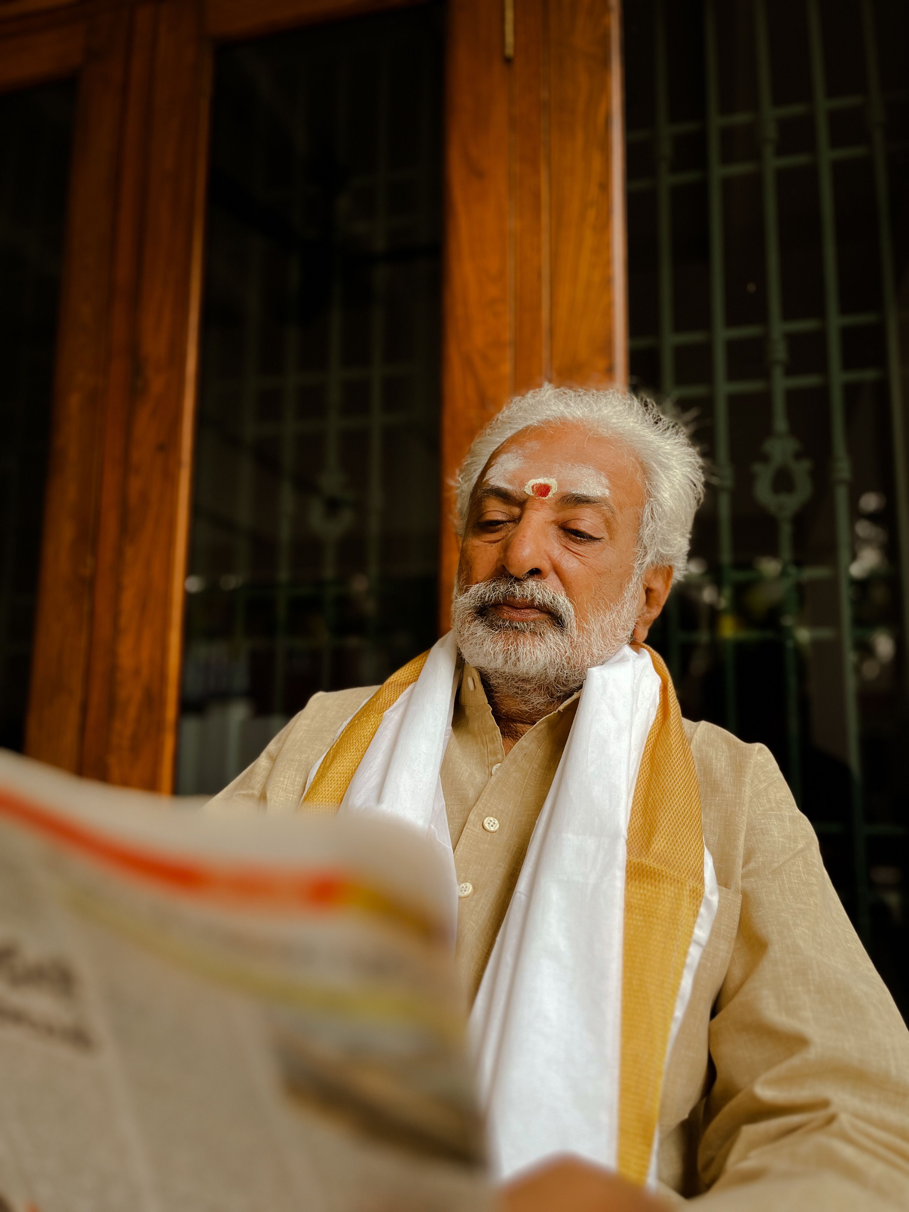 Senior man in traditional Indian clothing reading a newspaper, embodying cultural heritage.