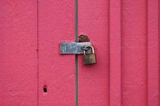 Close-up of a rusty padlock securing a vibrant pink metal door, showing wear.