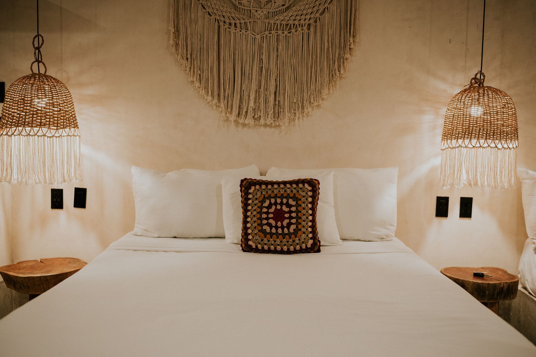 Warm bedroom with neutral bedding, macrame wall decor, woven lampshades and a wood nightstand