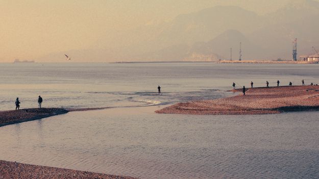 Serene beach setting with people fishing at sunrise along a calm shoreline.