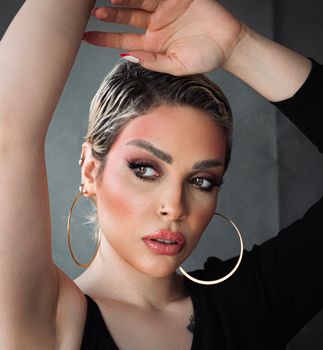Portrait of a stylish woman with bold makeup and large hoops posing confidently.