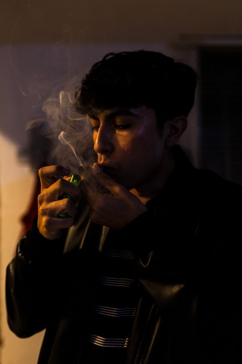 Free A young man in a black jacket lights a smoking pipe indoors at night. Stock Photo