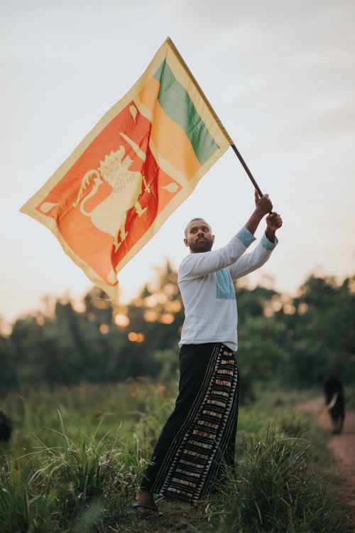 Free A man waves the Sri Lankan flag in a lush field during sunset, symbolizing pride and patriotism. Stock Photo