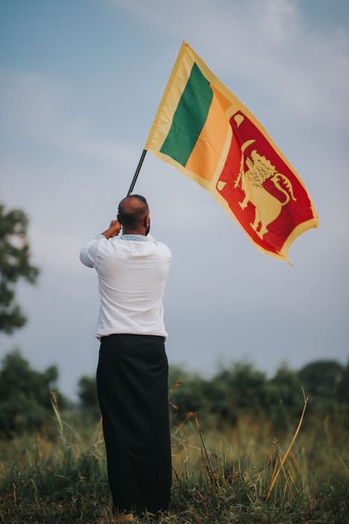 Free A man in traditional attire waving the Sri Lankan flag in a rural outdoor setting. Stock Photo
