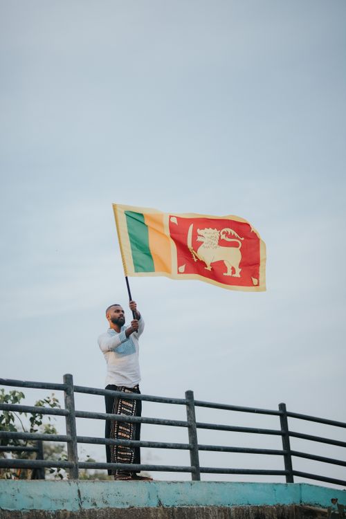 Free A man in traditional clothing waves the Sri Lankan flag on a bridge outdoors. Stock Photo