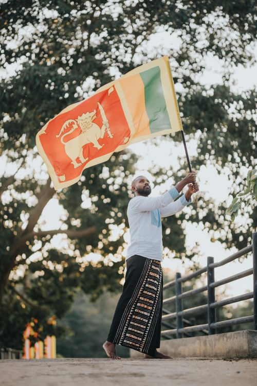 Free A man in traditional clothing waving the Sri Lankan flag outdoors. Stock Photo