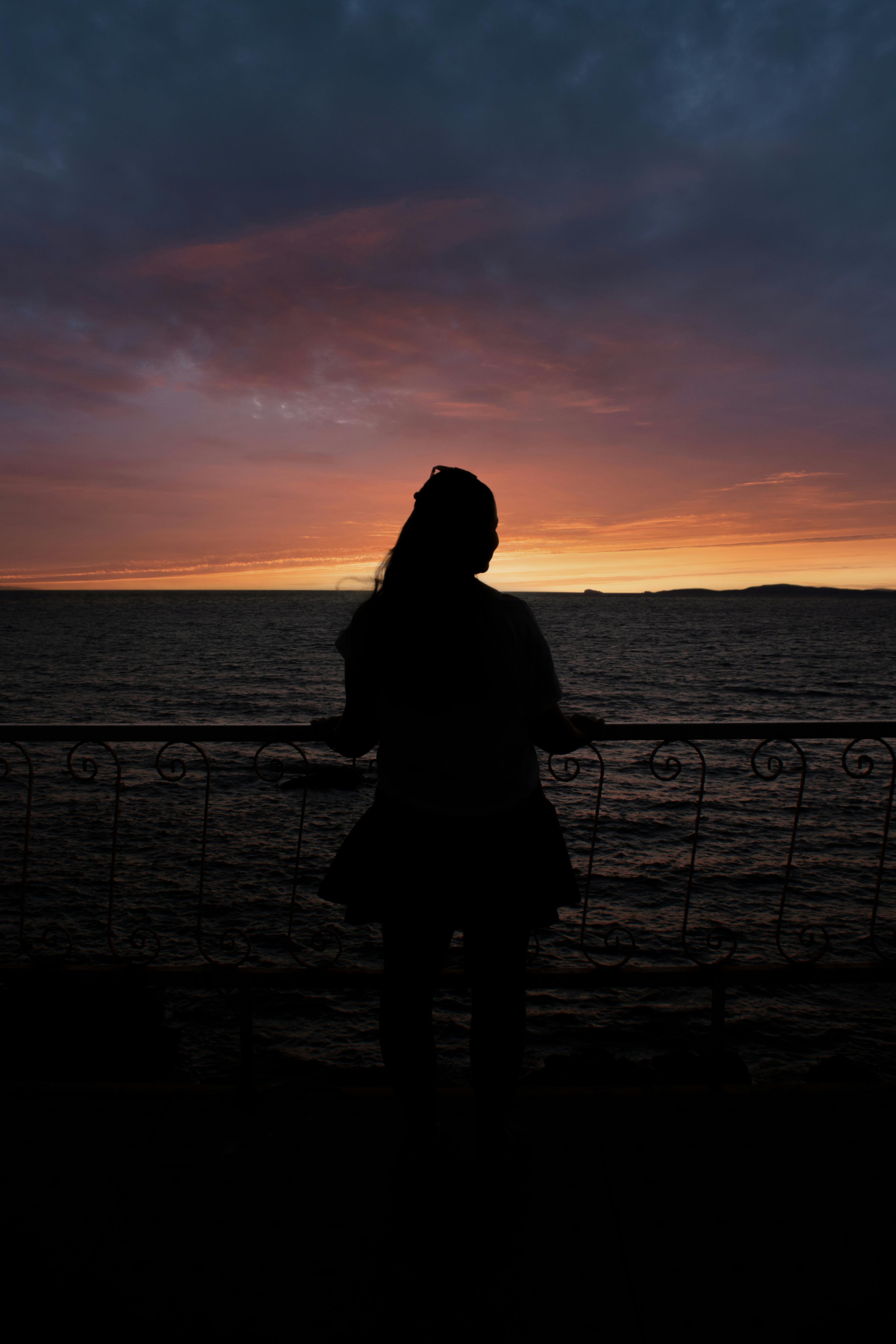 Female silhouette against a vibrant İzmir sunset over the Aegean Sea, Turkey.