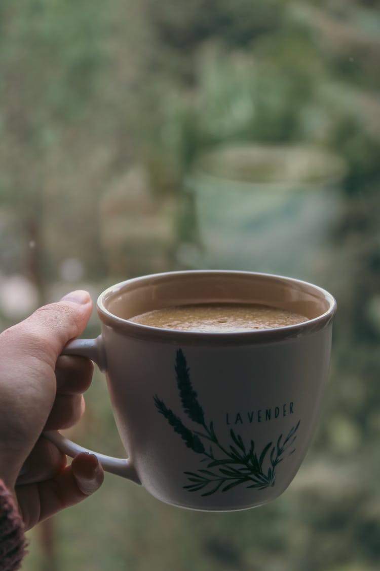 Hand Holding Coffee Cup By Window Pane