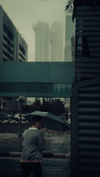 A man walks with an umbrella in rainy Dubai, capturing the city's moody urban atmosphere.
