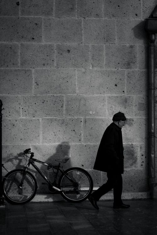 Free A man walks past a bicycle against a textured stone wall in an urban setting. Stock Photo
