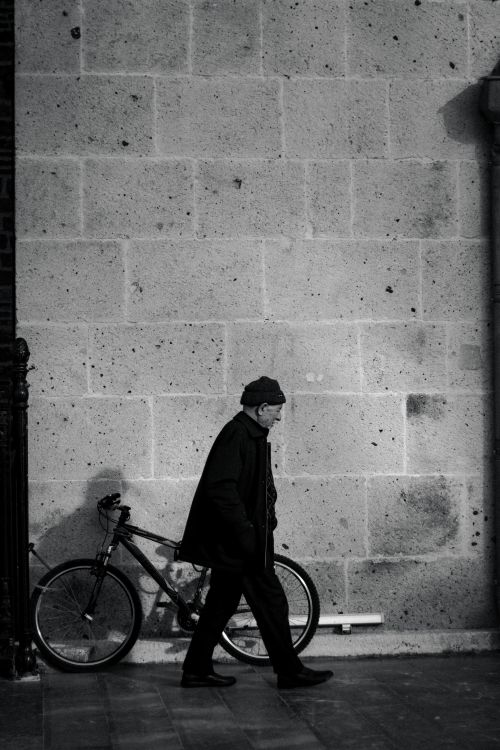 Free Monochrome image of a man walking past a bicycle against a city wall. Stock Photo