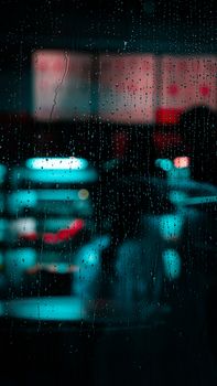 Raindrops on a window with blurred city lights in Dubai, creating a moody urban night scene.