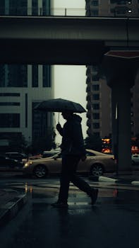 Silhouette of a man walking with an umbrella on a rainy street in Dubai, showcasing the city's urban landscape.