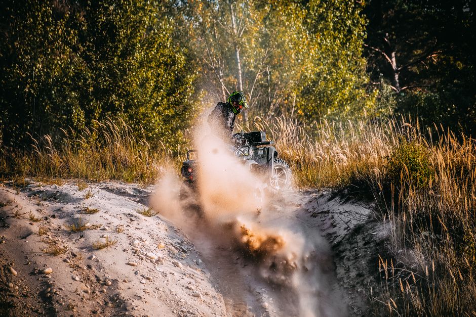 An ATV rider kicks up sand as they speed through a sandy landscape, showcasing thrilling outdoor adventure.