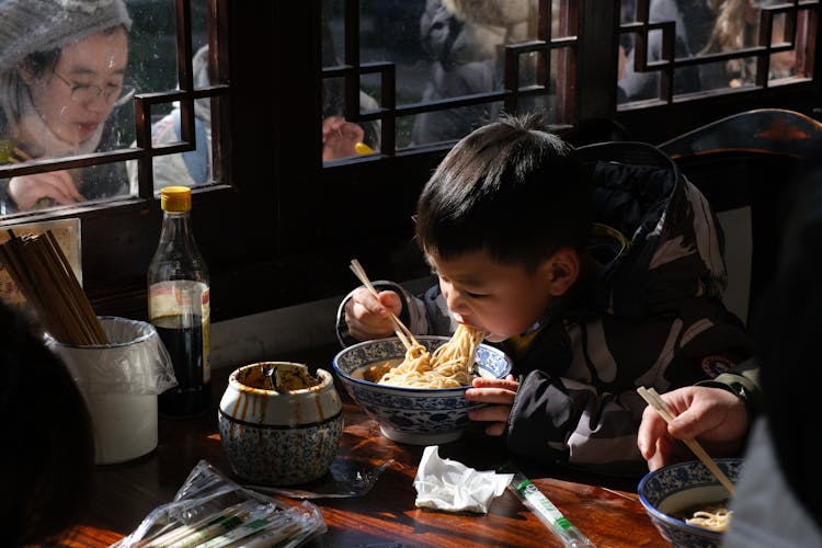 Photo Of A Child Eating Noodles With Chopsticks