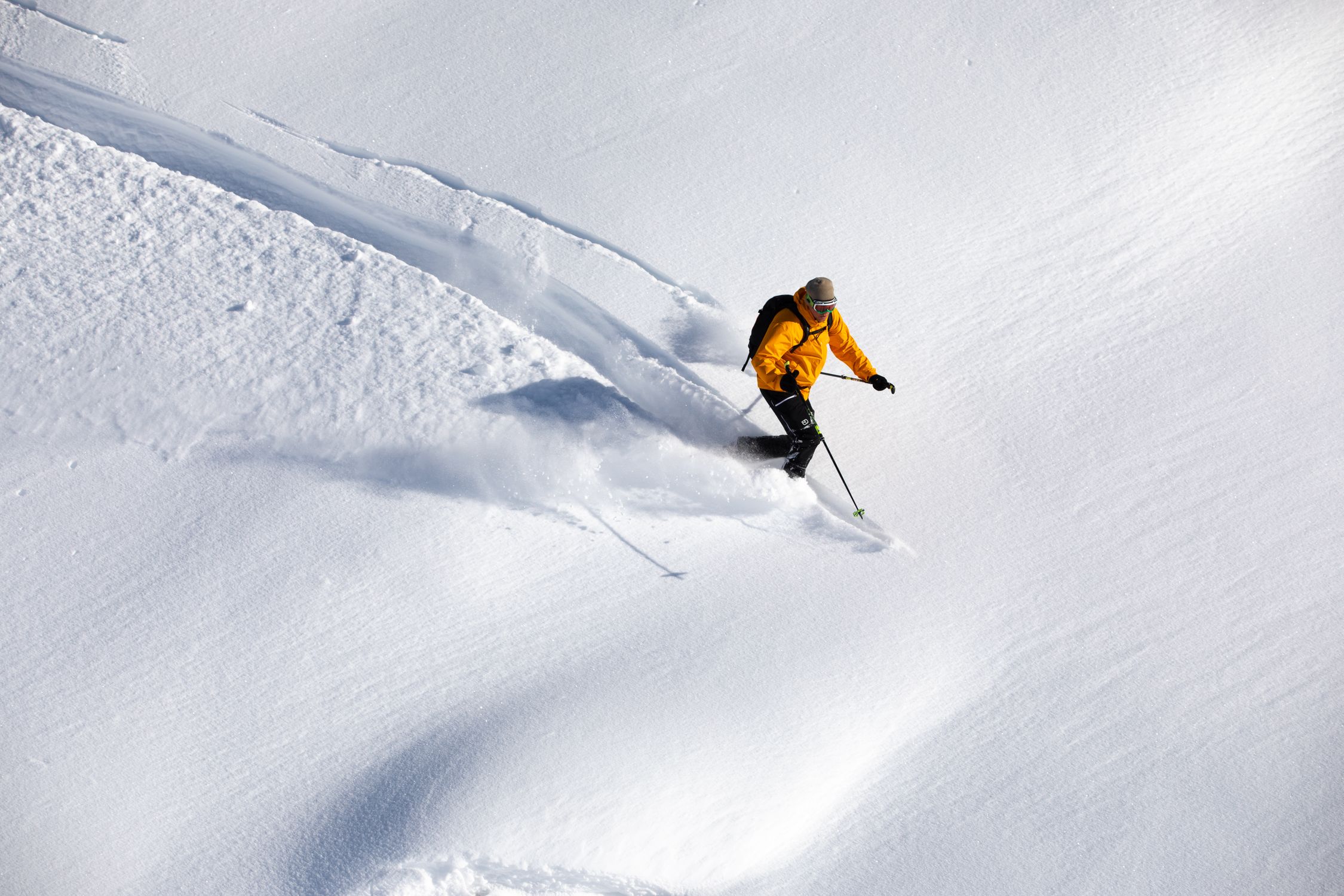 Skier in a yellow jacket descending a steep snowy backcountry slope surrounded by deep powder Skier in a yellow jacket descending a steep snowy backcountry slope surrounded by deep powder
