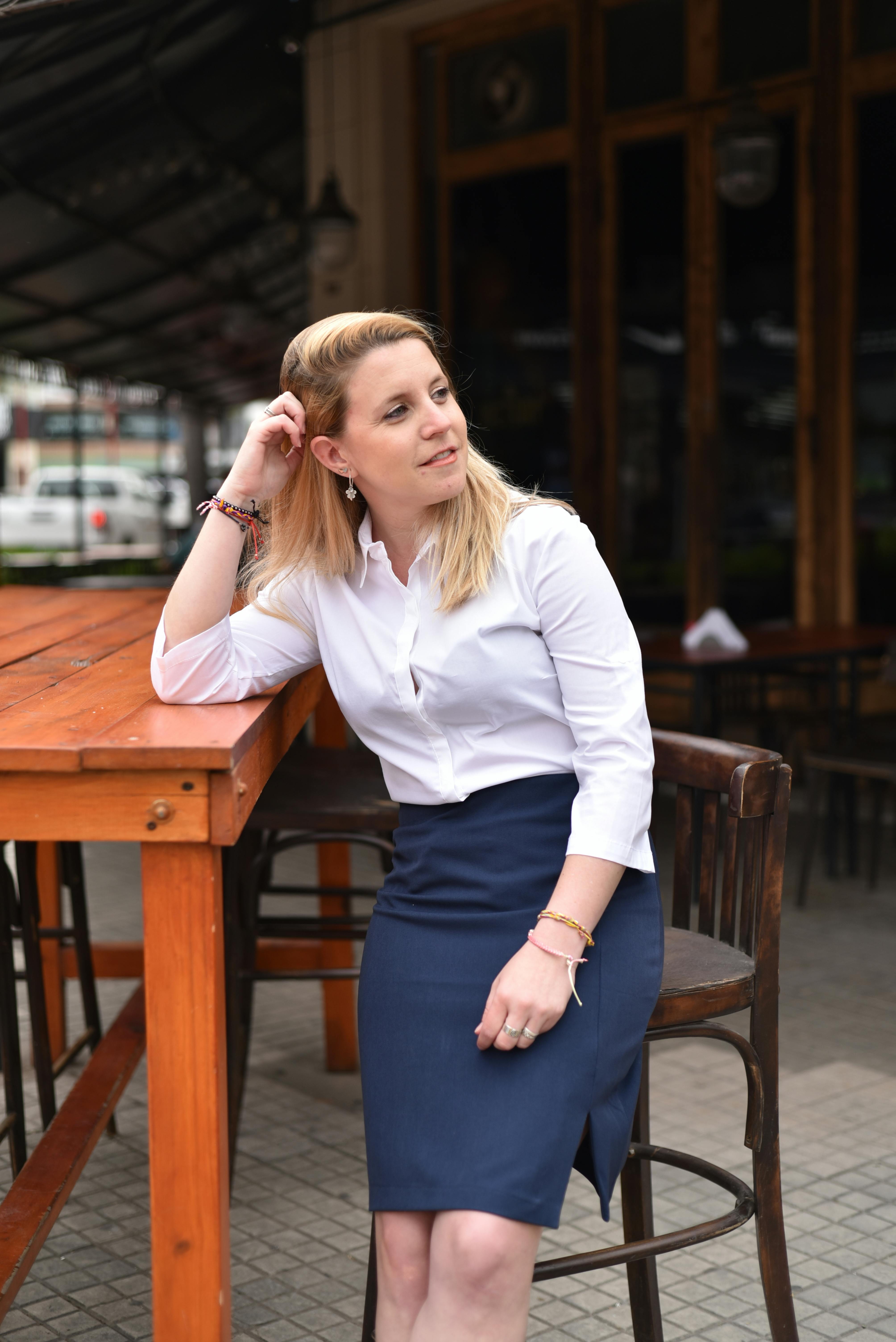 Businesswoman in a white blouse and blue skirt enjoys a break at an outdoor cafe setting.