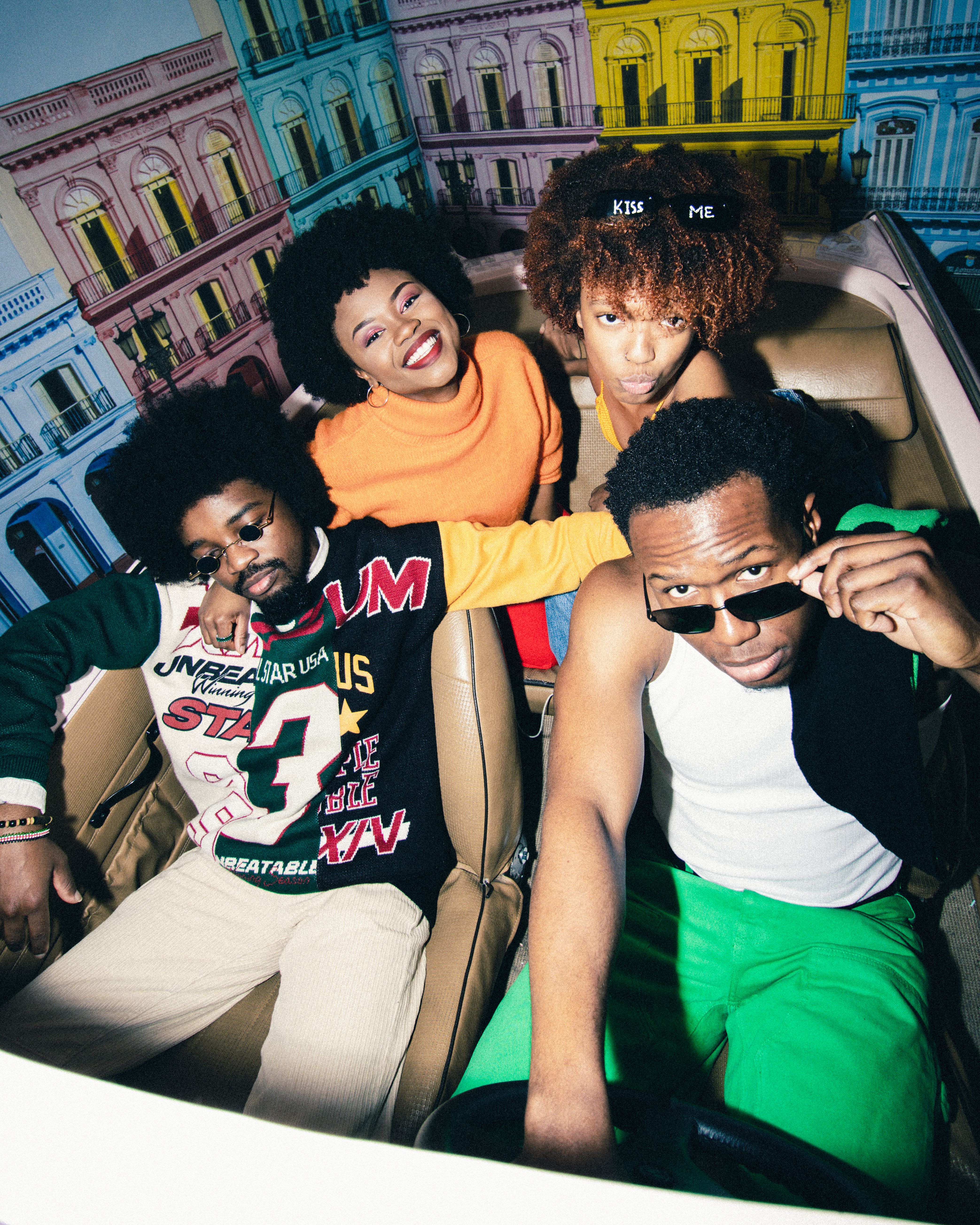 Group of friends posing inside a vibrant car, exuding a playful and retro vibe.