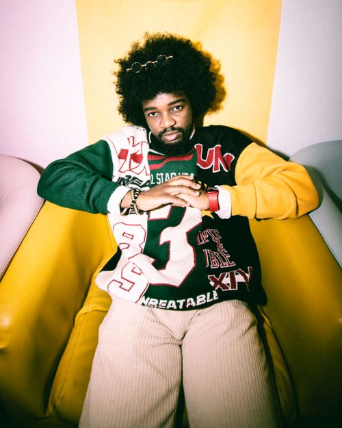 Free Man with afro hair sitting and relaxing in a vibrant room wearing casual clothing. Stock Photo