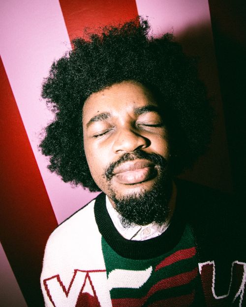 Free A serene close-up of an afro-haired man enjoying a moment against a colorful striped wall. Stock Photo