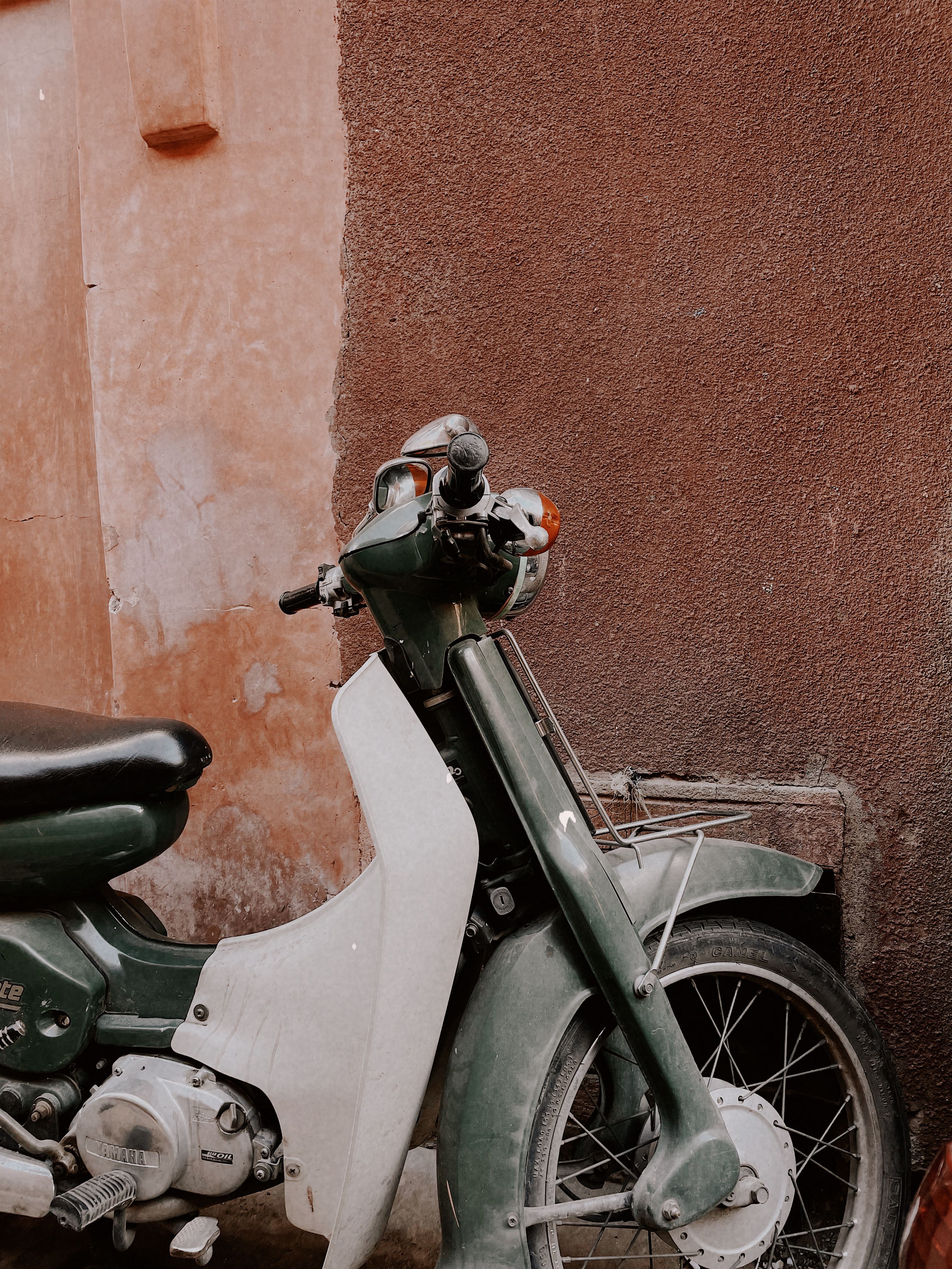 A classic green scooter parked against a brown wall in Marrakesh, Morocco.