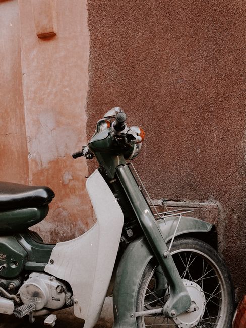 A classic green scooter parked against a brown wall in Marrakesh, Morocco.