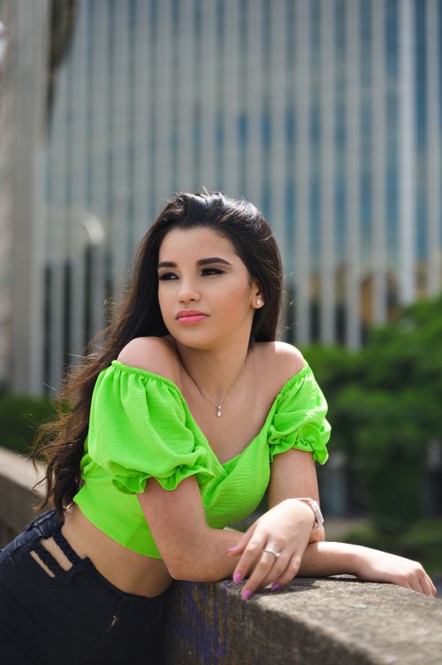 Free A stylish young woman poses outdoors against an urban backdrop in a vibrant green crop top. Stock Photo