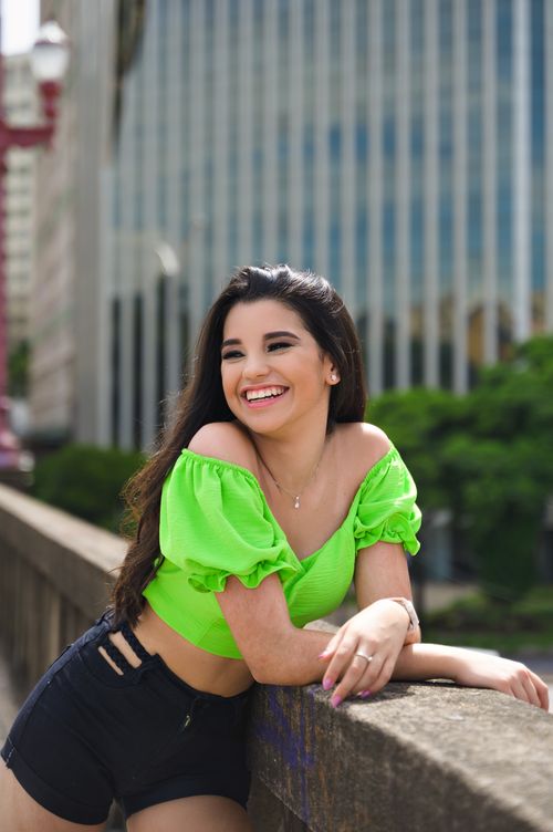 Free A young woman in a green crop top smiles brightly while posing outdoors on a city rooftop. Stock Photo