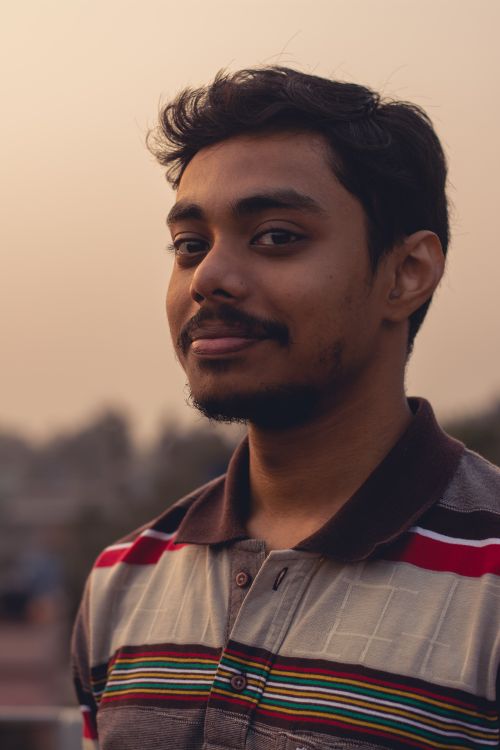 Free Portrait of a young man wearing a striped polo shirt outdoors at sunset, exuding calm confidence. Stock Photo