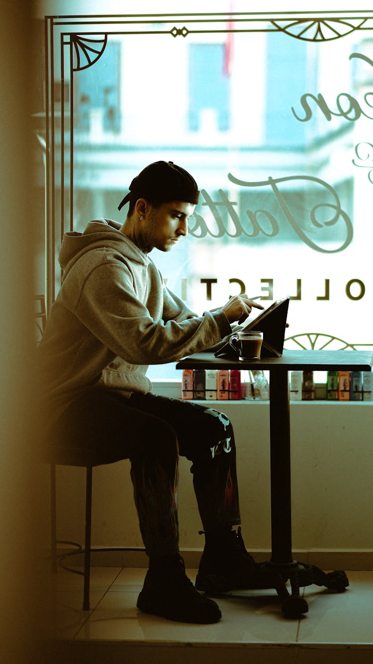 A Man Sitting Inside The Coffee Shop While Using His Tablet