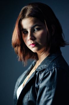 Fashion portrait of a woman in a black leather jacket with a dark background.