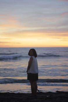 Woman standing on beach during sunset, captured in a tranquil sea background.