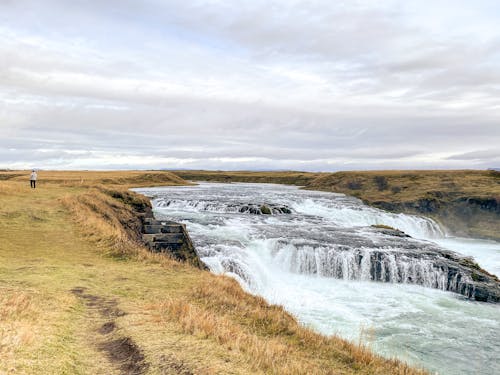 A Waterfalls Streaming on River Between Grass Field