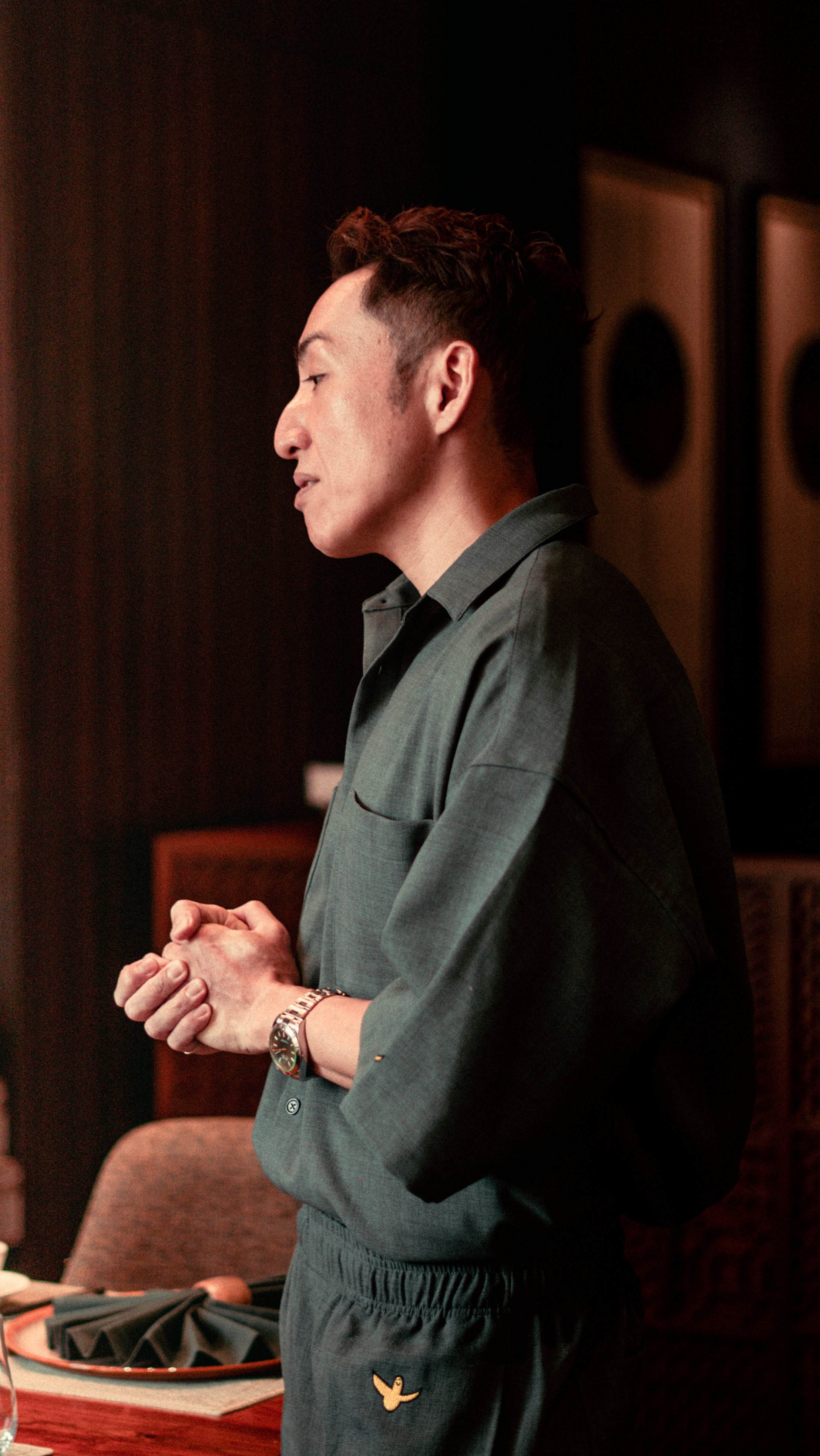 Profile view of a stylish man clasping hands in thoughtful pose indoors.