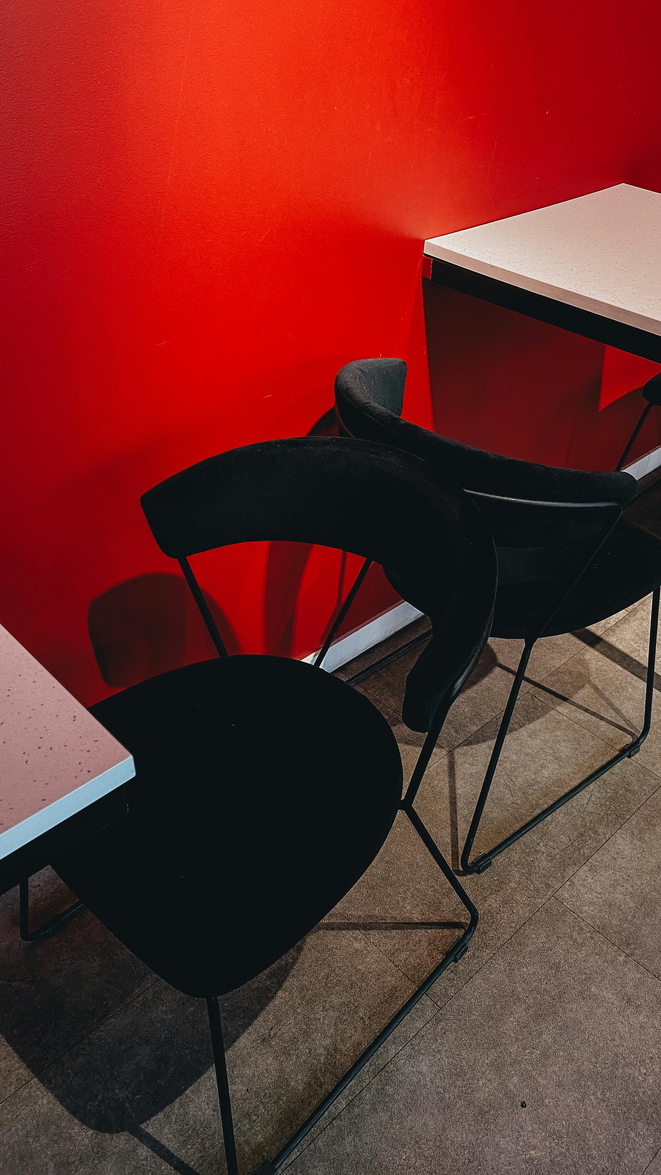 A modern, minimalist setting with dark chairs against a vibrant red wall and sleek tables.