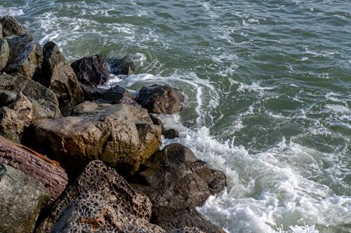 Free Close-up of rugged rocks on a coastline with waves crashing, depicting nature's power and beauty. Stock Photo