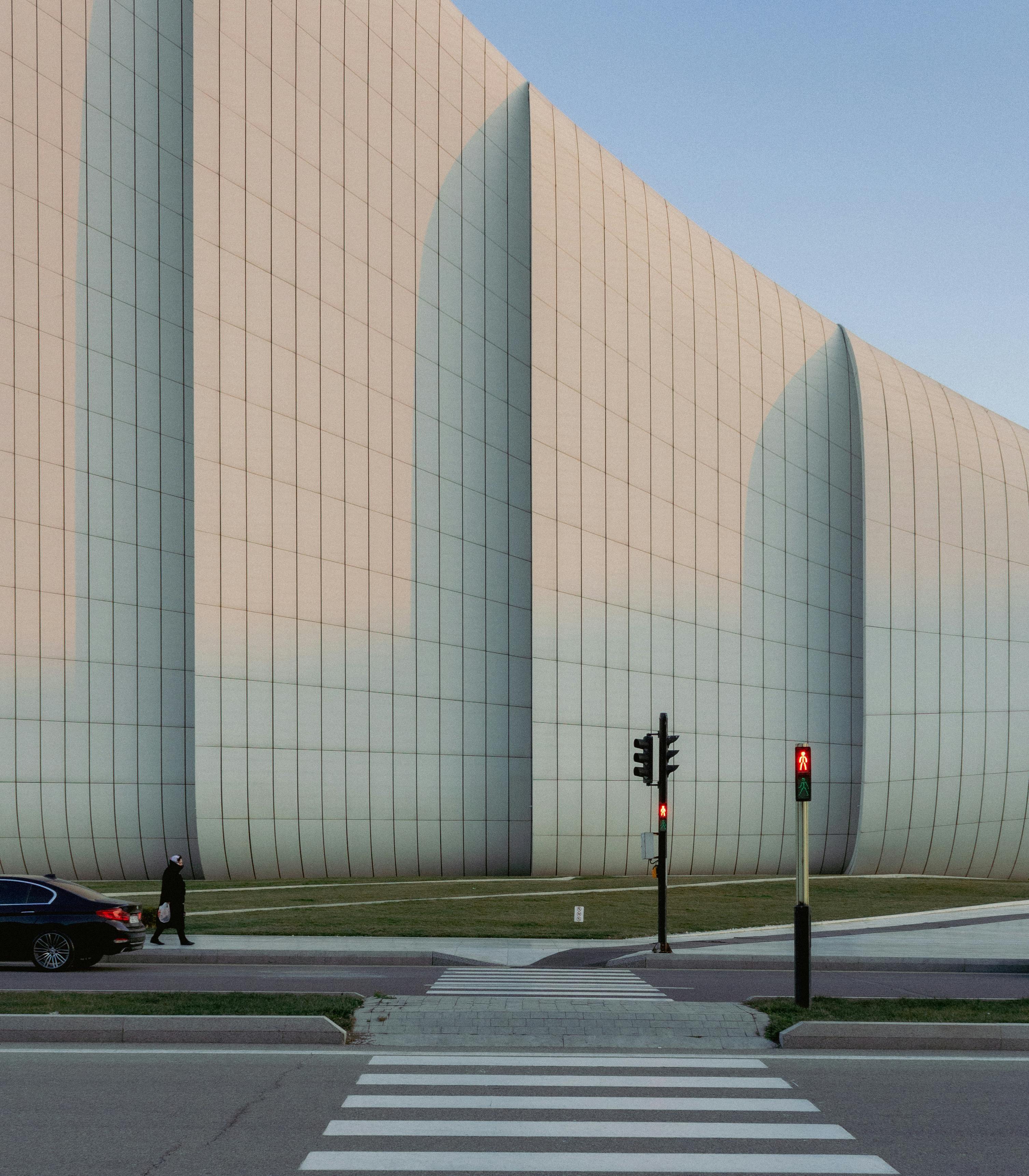 Modern architectural facade with crosswalk and red traffic light during day.