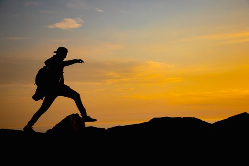 Free Silhouette of a man hiking over rocks against a vibrant sunset sky. Stock Photo