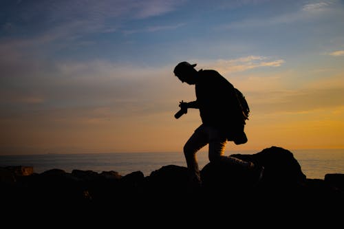 Silhouette of Man Walking on Rocks on Sunset 