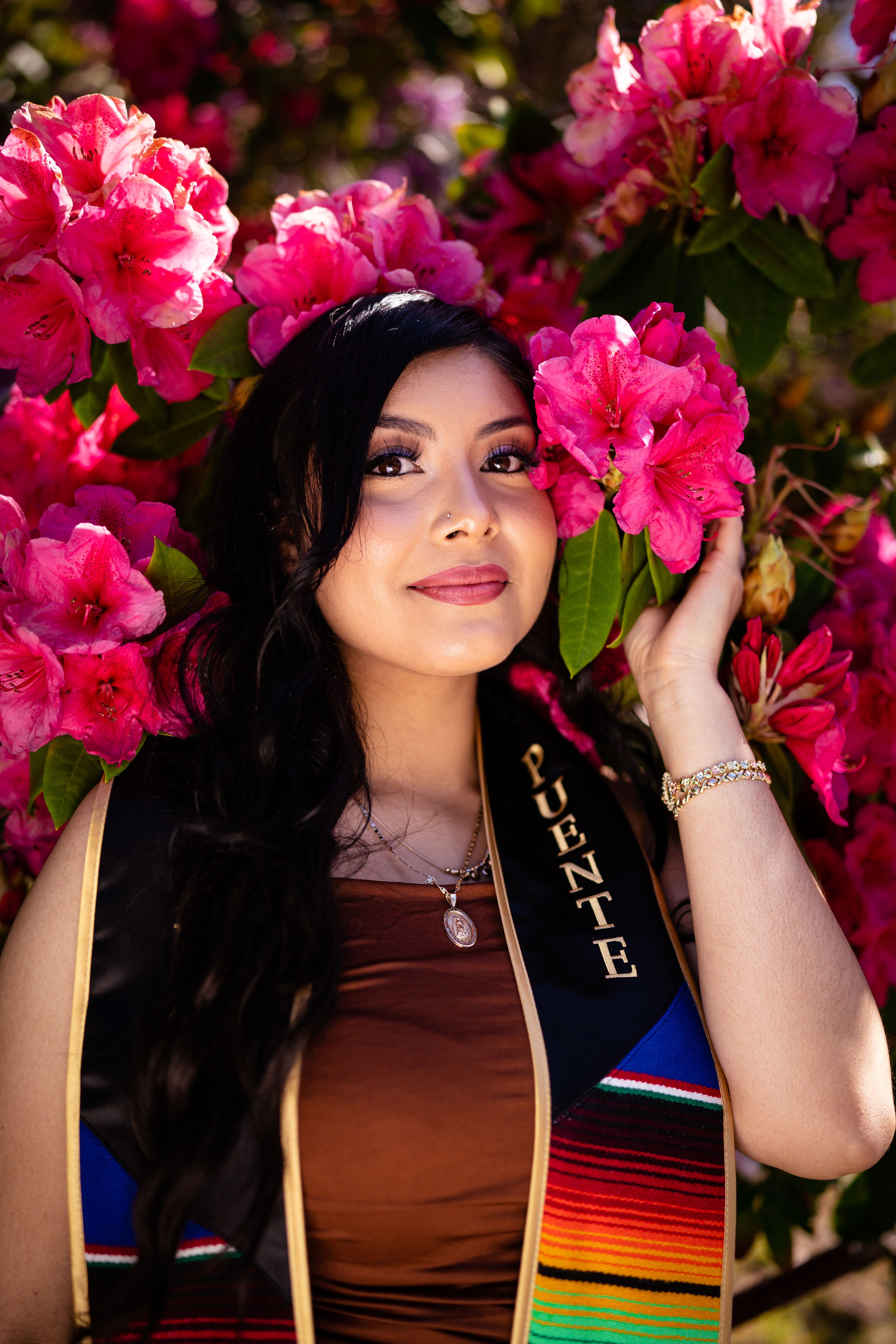 Smiling graduate poses with vibrant flowers, capturing a joyful outdoor scene.