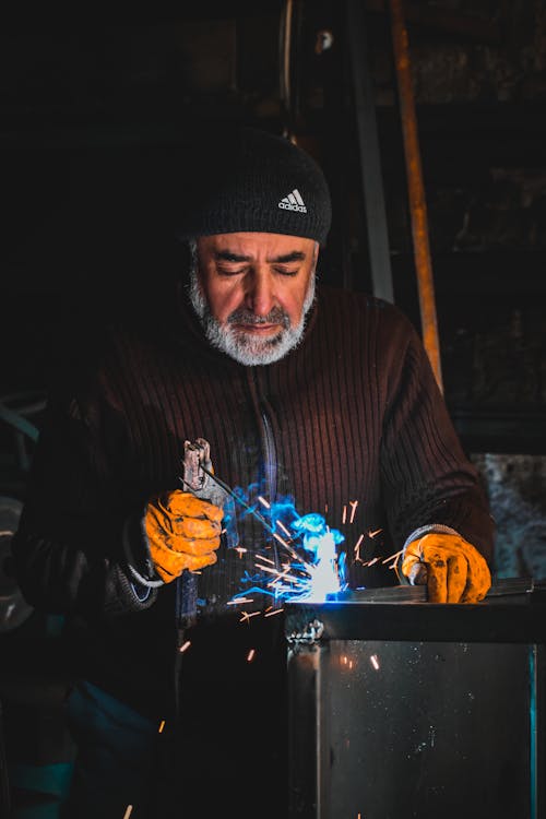 Old Bearded Man Welding Metal in Dark