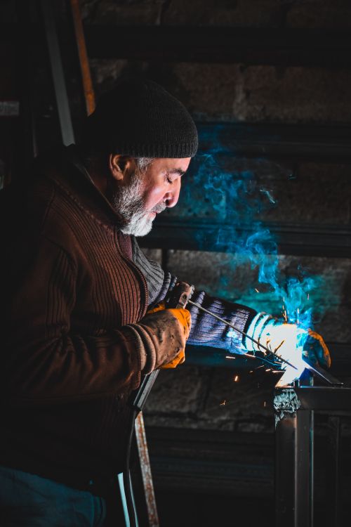 Free Focused industrial worker welding a metal frame with bright sparks indoors. Stock Photo