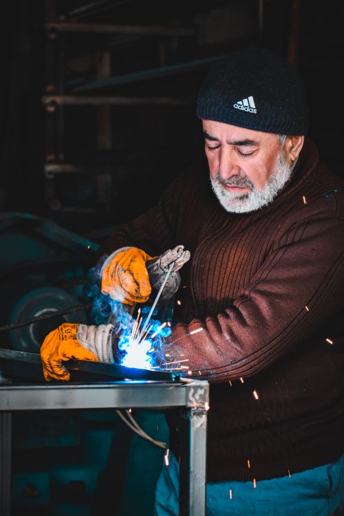 Free Elderly man welding in a workshop, creating sparks and focusing on his craft. Stock Photo