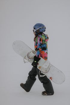 A snowboarder in vibrant winter gear carrying a snowboard across a snowy landscape.